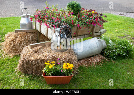 A rustic old wooden wheelbarrow filled with colorful flowers, Dairy milking farm equipment, milk churns, straw bales, at Southport Flower Show, Victoria Park, UK Stock Photo