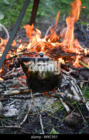 old shiny metal kettle basks on a fire, travel vacation weekend on a summer day, vertical photo Stock Photo