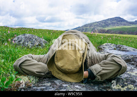 tired traveler in the mountains - a man in a hat and camp clothes resting lying on his back on a mountain plateau Stock Photo