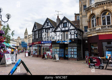 3 shops on Fore street Trowbridge in a Mock Tudor building with market day traders visible in the street Stock Photo