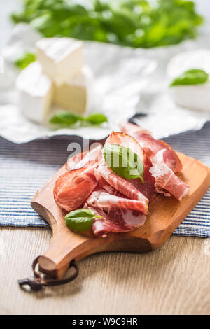 Pork ham prosciutto and camembert or brie cheese  with basil leaves on table Stock Photo