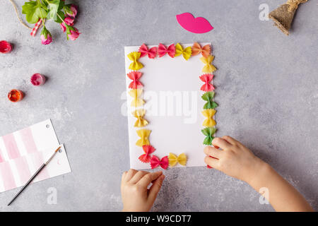 Paper crafts for mother day, 8 march or birthday. Small child doing a bouquet of flowers out of colored paper and colored pasta. Stock Photo