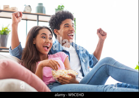 Black teen couple watching tv, sitting with popcorn at home Stock Photo