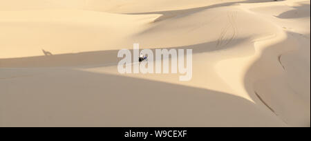 Mui Ne, Vietnam - June 2019: off-road ATV quad bike driving through desert sand dunes at sunrise. Stock Photo