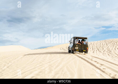 Mui Ne, Vietnam - June 2019: off-road vintage soviet car driving through desert sand dunes at sunrise. Stock Photo