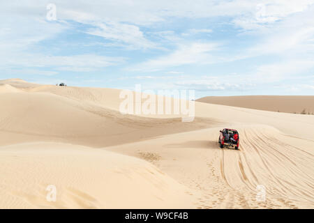 Mui Ne, Vietnam - June 2019: off-road red car driving through desert sand dunes at sunrise Stock Photo