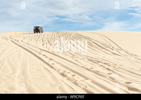 Mui Ne, Vietnam - June 2019: off-road vintage soviet car driving through desert sand dunes at sunrise. Stock Photo