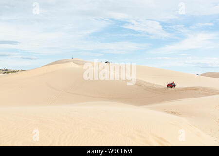 Mui Ne, Vietnam - June 2019: off-road red car driving through desert sand dunes at sunrise Stock Photo