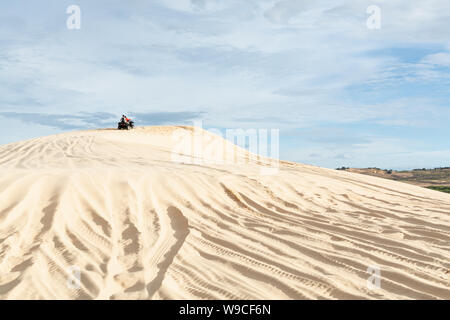 Mui Ne, Vietnam - June 2019: off-road ATV quad bike driving through desert sand dunes at sunrise. Stock Photo