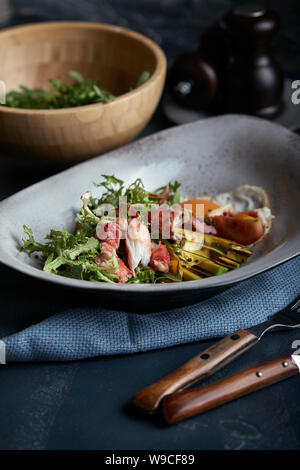 Salad with crab and avocado on a dark background. Arugula salad leaves seasoned with sauce on white wine with crab meat and grilled avocado in soft Stock Photo