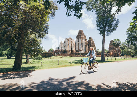 Young woman riding bicycle next to ancient Pre Rup temple ruins in Angkor Wat complex, Cambodia Stock Photo