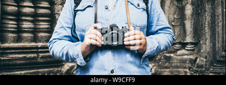 Woman in denim jeans shirt holding vintage film camera with Angkor Wat temple on background, Cambodia Stock Photo