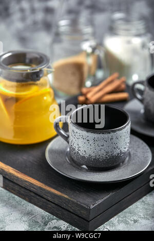 Transparent glass teapot with chitrus tea and cups, tea set on a wooden table. Close up, gray background, soft light. Stock Photo