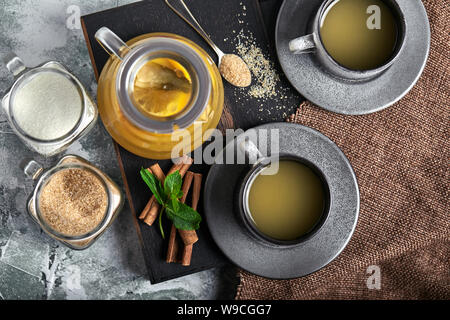 Transparent glass teapot with chitrus tea and cups, tea set on a wooden table. Close up, gray background, soft light. Stock Photo