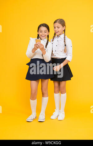 Internet is wonderful resource but access to it has hazards for kids. Girls school uniform using smartphone. Schoolgirls use mobile phone or smartphone to share photos. School application smartphone. Stock Photo