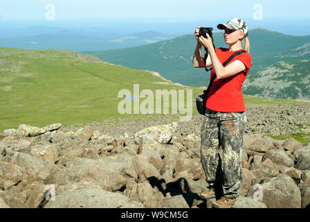 girl photographer hiker takes a picture standing on a high mountainside in the background of a mountain landscape Stock Photo