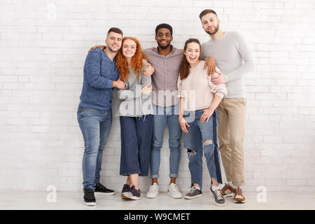Happy friends embracing and posing to camera over white wall Stock Photo