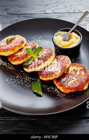 german quark Potato pancakes - Quarkkeulchen sprinkled with powdered sugar, decorated with mint leaves on a black plate with apple sauce, view from ab Stock Photo
