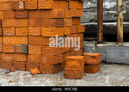 stack of bricks made of red clay on the background of some structures of a building under construction Stock Photo