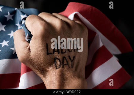 closeup of the raised fist of a young man with the text labor day handwritten in it, and the flag of the United States Stock Photo