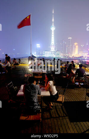 Customers talk on the open terrace of Bar Rouge at the Bund 18 as the night view of the Lujiazui Financial District in Pudong is seen in the backgroun Stock Photo