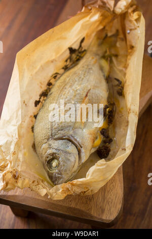 A Black Bream, Spondyliosoma cantharus, that has been cooked in a halogen oven en papillote. It was placed on baking paper with lemon slices, butter a Stock Photo