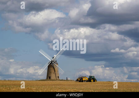 A bailer works in a field in front of Great Haseley windmill in Oxfordshire. Stock Photo