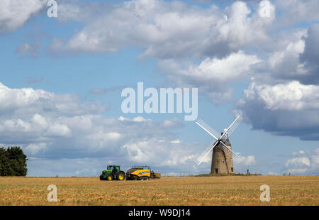A bailer works in a field in front of Great Haseley windmill in Oxfordshire. Stock Photo