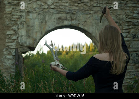 witch - young woman in black dress conducts some sinister pagan rite among ancient ruins, back view Stock Photo