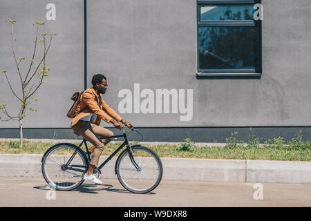 stylish african american businessman riding bicycle on sunny street Stock Photo