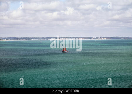 Sailing yacht with red sail goes on the turquoise sea, English Channel, United Kingdom
