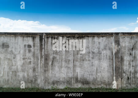 Old cracked gray cement or concrete wall with blue sky as background. Grunge plastered stucco  textured background. Stock Photo