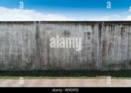 Old cracked gray cement or concrete wall with blue sky as background. Grunge plastered stucco  textured background. Stock Photo