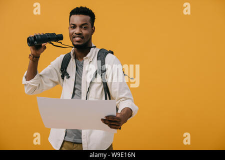 happy african american man holding binoculars and blank paper isolated on yellow Stock Photo