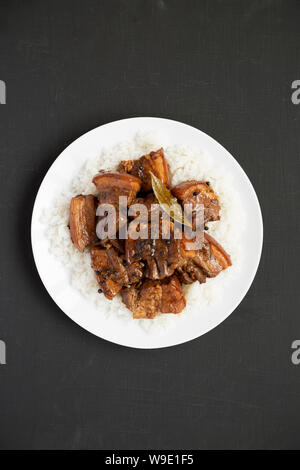 Homemade Filipino Adobo Pork with rice on a white plate over black background, top view. Asian food. Flat lay, overhead, from above. Stock Photo