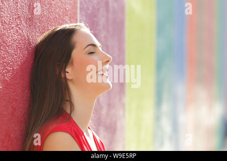 Side view portrait of a happy woman resting leaning in a colorful wall Stock Photo
