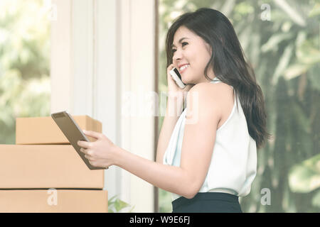 Young entrepreneur checking products stock on the smart tablet while talking to her customer at home office. Stock Photo