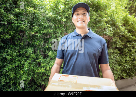 Asian delivery man smiling while holding a cardboard box delivery to his customer. Stock Photo