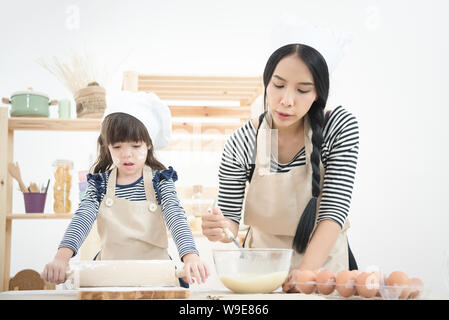 Asian mother and her daughter are preparing the dough to make a cake in the kitchen room on vacation.Photo series of Happy family concept. Stock Photo