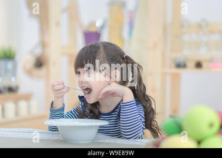 Cute little girl eating breakfast with cornflakes and milk in the morning. Photo series of family, kids and happy people concept. Stock Photo