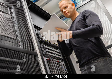 Male IT Engineer Using Tablet In Datacenter to Monitor Network and Servers Stock Photo