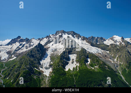 Mountain peaks with a glacier and the beginning of a mountain stream that flows through a pine forest. North Caucasus, Russia Stock Photo