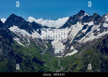 Mountain peaks with a glacier and the beginning of a mountain stream that flows through a pine forest. North Caucasus, Russia Stock Photo