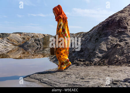 girl of oriental appearance in a sari and hijab with a jug by the lake in the desert Stock Photo