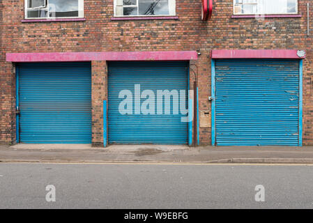 Row three blue painted roller shutter doors in Birmingham's historic Gun Quarter in Aston, Birmingham Stock Photo