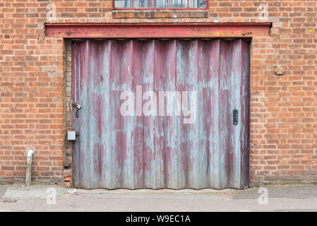 Old worn red roller shutter door on factory with flaking paint Stock Photo