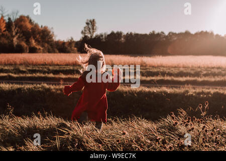 Little girl outdoors in autumn holds tiny pumpkin running in a field Stock Photo