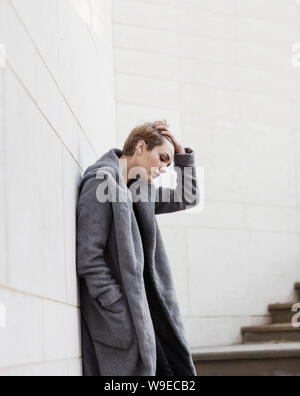 Young woman in a gray coat straightens her hair while standing on the Stock Photo