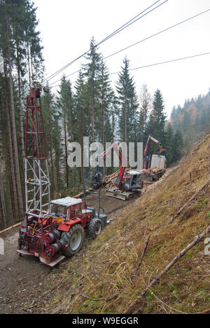 Timber harvesting with skyline crane and manipulator in autumnal misty forest in steep terrain of low mountain range of the Austrian Alps. Stock Photo