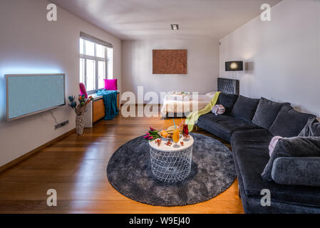 Grey sofa and covered bed in living room. Tv on the wall. Stock Photo